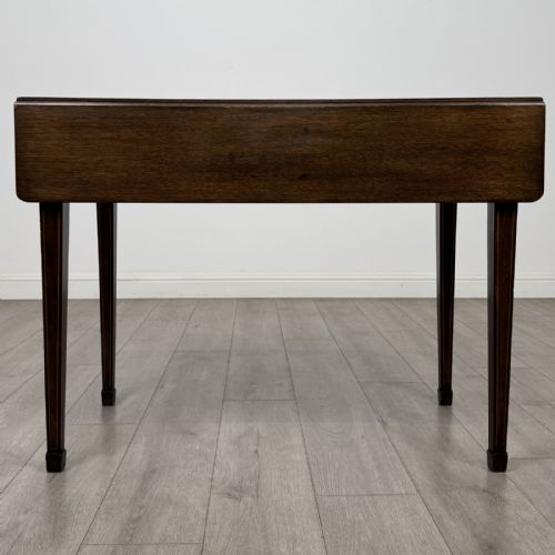 fig 1. A dark brown mahogany Pembroke table featuring two drop flaps, a front drawer with boxwood line inlay, two brass ring handles, and square tapered legs ending in spade feet.