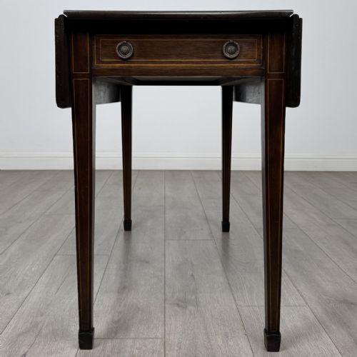 fig 3. A dark brown mahogany Pembroke table featuring two drop flaps, a front drawer with boxwood line inlay, two brass ring handles, and square tapered legs ending in spade feet.