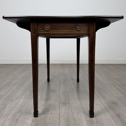fig 4. A dark brown mahogany Pembroke table featuring two drop flaps, a front drawer with boxwood line inlay, two brass ring handles, and square tapered legs ending in spade feet.