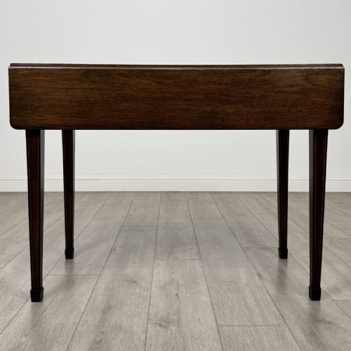 fig 6. A dark brown mahogany Pembroke table featuring two drop flaps, a front drawer with boxwood line inlay, two brass ring handles, and square tapered legs ending in spade feet.