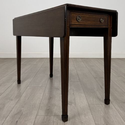 fig 7. A dark brown mahogany Pembroke table featuring two drop flaps, a front drawer with boxwood line inlay, two brass ring handles, and square tapered legs ending in spade feet.