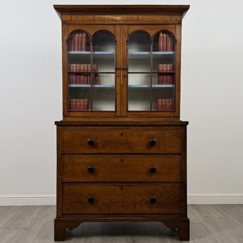 fig 1. An 18th-century Georgian golden oak glazed bookcase resting upon a chest of three long drawers with turned wooden handles and shaped bracket feet.