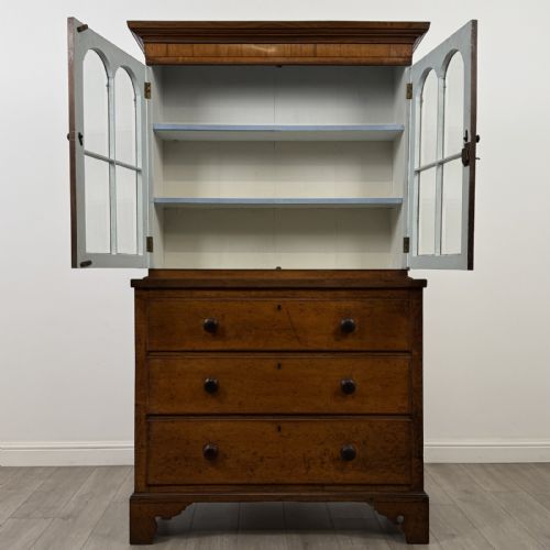 fig 2. An 18th-century Georgian golden oak glazed bookcase resting upon a chest of three long drawers with turned wooden handles and shaped bracket feet.
