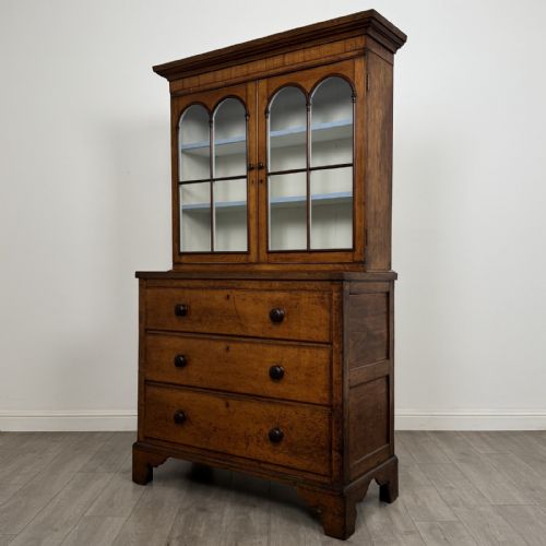 fig 3. An 18th-century Georgian golden oak glazed bookcase resting upon a chest of three long drawers with turned wooden handles and shaped bracket feet.