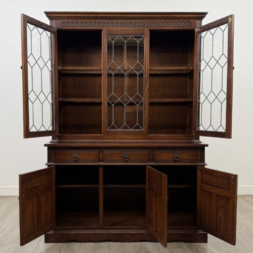 fig 1. A dark oak display cabinet featuring three leaded glass doors, three drawers, and three carved panelled cupboards with brass handles.