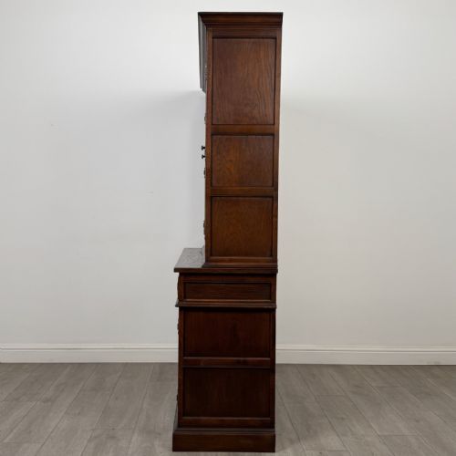 fig 3. A dark oak display cabinet featuring three leaded glass doors, three drawers, and three carved panelled cupboards with brass handles.