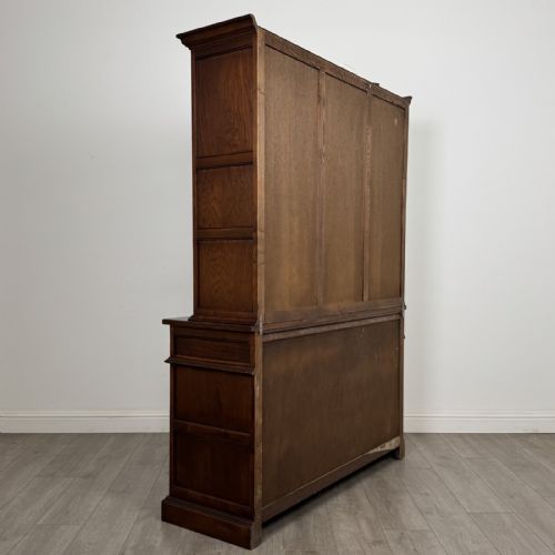 fig 4. A dark oak display cabinet featuring three leaded glass doors, three drawers, and three carved panelled cupboards with brass handles.