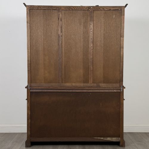 fig 5. A dark oak display cabinet featuring three leaded glass doors, three drawers, and three carved panelled cupboards with brass handles.