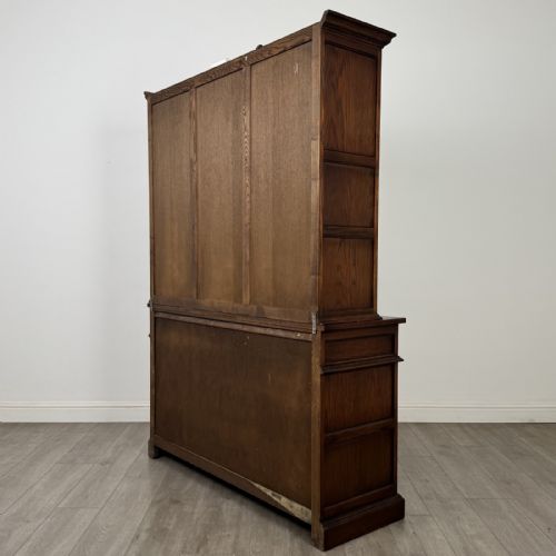 fig 6. A dark oak display cabinet featuring three leaded glass doors, three drawers, and three carved panelled cupboards with brass handles.