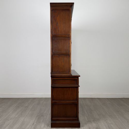 fig 7. A dark oak display cabinet featuring three leaded glass doors, three drawers, and three carved panelled cupboards with brass handles.