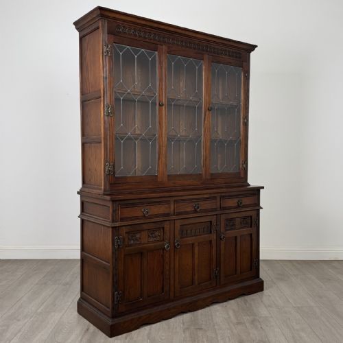 fig 8. A dark oak display cabinet featuring three leaded glass doors, three drawers, and three carved panelled cupboards with brass handles.