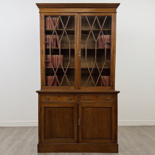 fig 1. A Victorian golden oak two-part glazed bookcase featuring geometric astragal glazing, a dentil cornice, two drawers, and a panelled base cupboard.