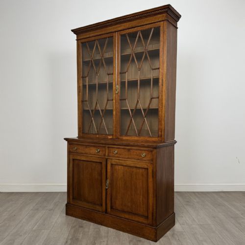 fig 3. A Victorian golden oak two-part glazed bookcase featuring geometric astragal glazing, a dentil cornice, two drawers, and a panelled base cupboard.