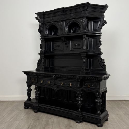 fig 1. An ornate ebonised dark wood Victorian sideboard featuring upper tier shelves with carved arches, lion masks, and lower drawers with brass drop handles.