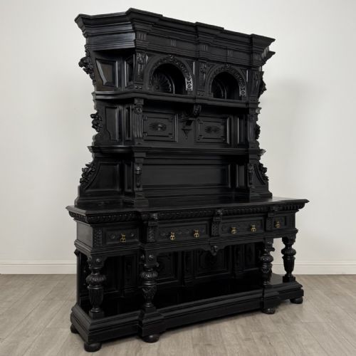 fig 7. An ornate ebonised dark wood Victorian sideboard featuring upper tier shelves with carved arches, lion masks, and lower drawers with brass drop handles.