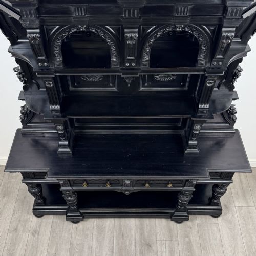 fig 8. An ornate ebonised dark wood Victorian sideboard featuring upper tier shelves with carved arches, lion masks, and lower drawers with brass drop handles.