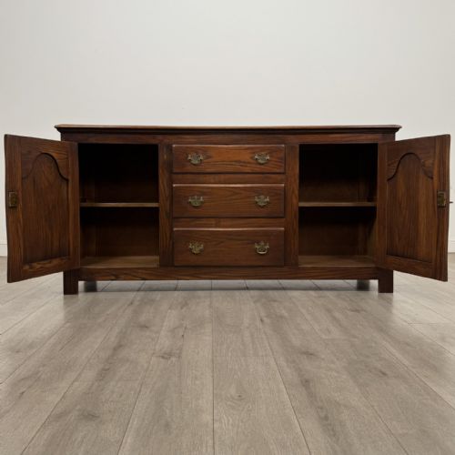fig 1. A dark oak sideboard featuring three central drawers flanked by two arched panel cupboard doors with brass handles.