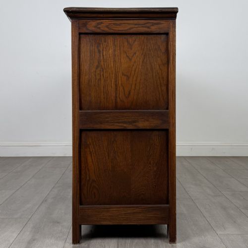 fig 3. A dark oak sideboard featuring three central drawers flanked by two arched panel cupboard doors with brass handles.
