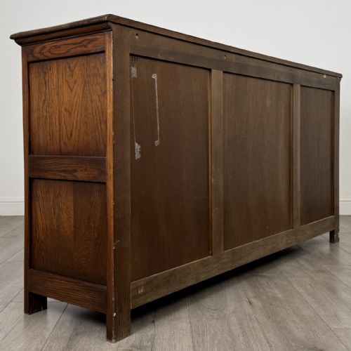 fig 4. A dark oak sideboard featuring three central drawers flanked by two arched panel cupboard doors with brass handles.