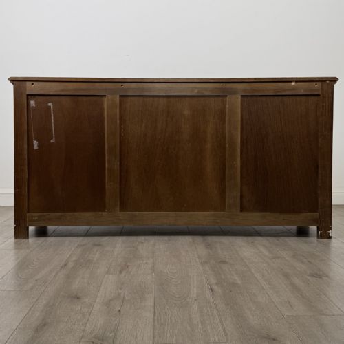 fig 5. A dark oak sideboard featuring three central drawers flanked by two arched panel cupboard doors with brass handles.