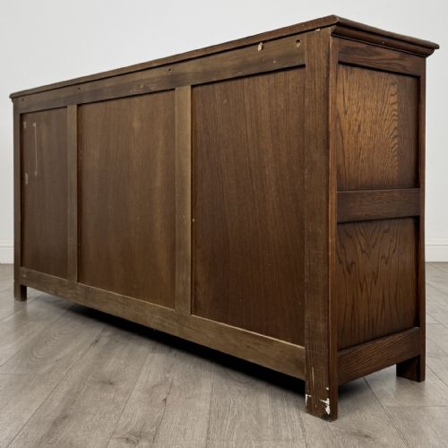 fig 6. A dark oak sideboard featuring three central drawers flanked by two arched panel cupboard doors with brass handles.