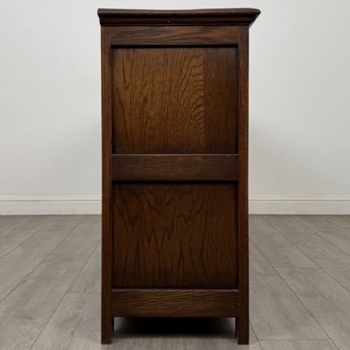 fig 7. A dark oak sideboard featuring three central drawers flanked by two arched panel cupboard doors with brass handles.