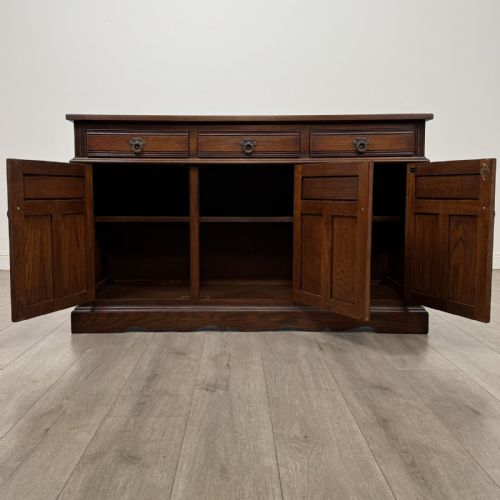 fig 1. A dark oak sideboard featuring three drawers above three cupboard doors decorated with carved floral and arcaded panels and ornamental drop handles.