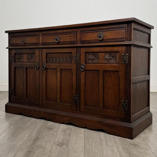 fig 2. A dark oak sideboard featuring three drawers above three cupboard doors decorated with carved floral and arcaded panels and ornamental drop handles.