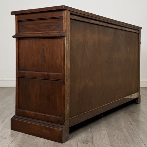 fig 4. A dark oak sideboard featuring three drawers above three cupboard doors decorated with carved floral and arcaded panels and ornamental drop handles.