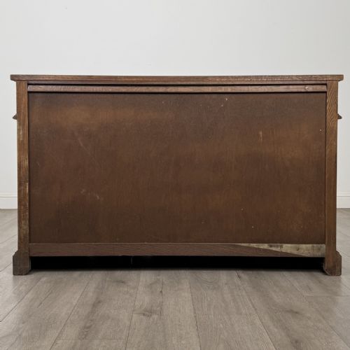 fig 5. A dark oak sideboard featuring three drawers above three cupboard doors decorated with carved floral and arcaded panels and ornamental drop handles.