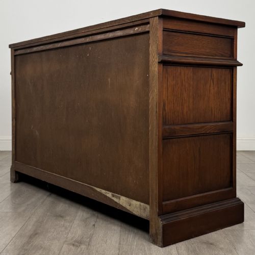fig 6. A dark oak sideboard featuring three drawers above three cupboard doors decorated with carved floral and arcaded panels and ornamental drop handles.