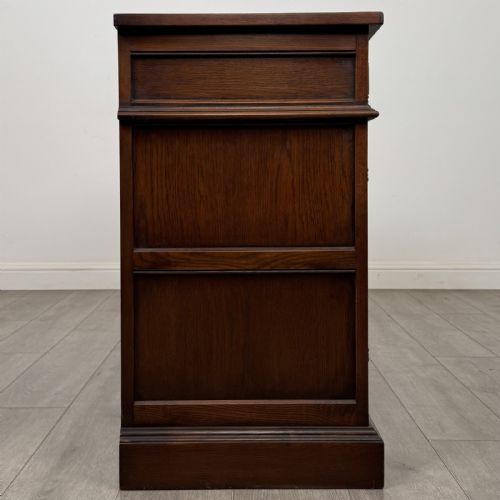 fig 7. A dark oak sideboard featuring three drawers above three cupboard doors decorated with carved floral and arcaded panels and ornamental drop handles.