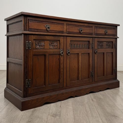 fig 8. A dark oak sideboard featuring three drawers above three cupboard doors decorated with carved floral and arcaded panels and ornamental drop handles.