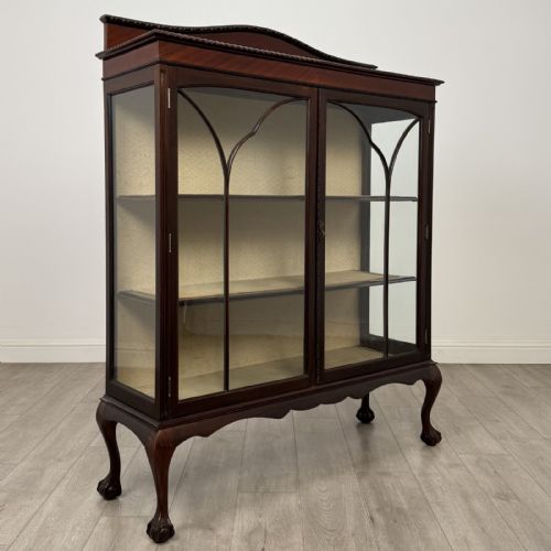 fig 8. An Edwardian dark mahogany display cabinet with twin astragal glazed doors, fabric-lined interior shelves, and cabriole legs with carved claw and ball feet.