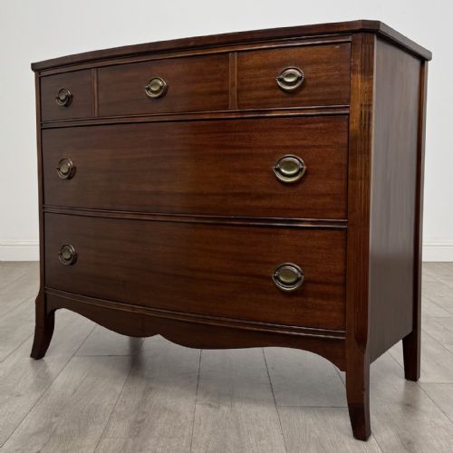 fig 1. A dark mahogany bow-fronted chest of drawers featuring brass oval ring handles, reeded side columns, and curved legs.