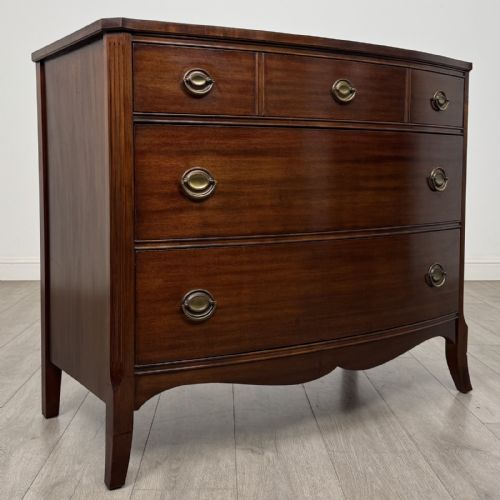 fig 7. A dark mahogany bow-fronted chest of drawers featuring brass oval ring handles, reeded side columns, and curved legs.