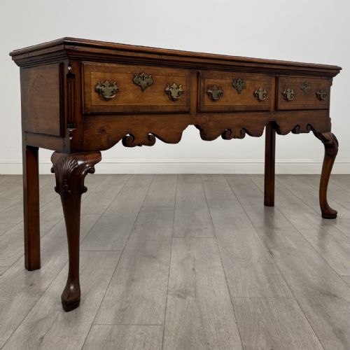 fig 7. A Queen Anne style elm dresser base featuring three drawers with brass handles, a shaped apron, and cabriole legs ending in pad feet.