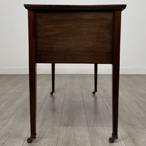 fig 2. An Edwardian mahogany writing table featuring three inlaid drawers, brass drop handles, square tapered legs, and brass castors.