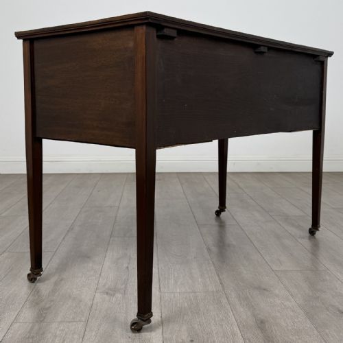 fig 3. An Edwardian mahogany writing table featuring three inlaid drawers, brass drop handles, square tapered legs, and brass castors.