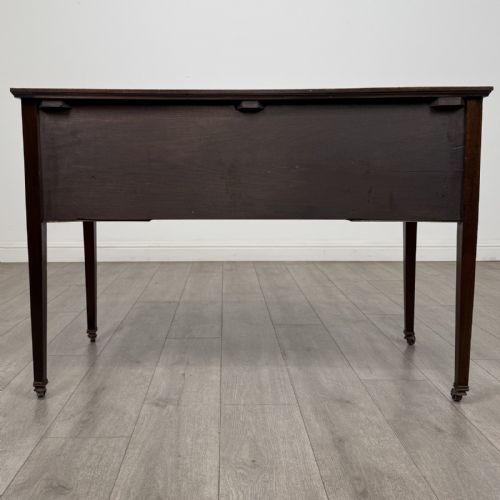 fig 4. An Edwardian mahogany writing table featuring three inlaid drawers, brass drop handles, square tapered legs, and brass castors.