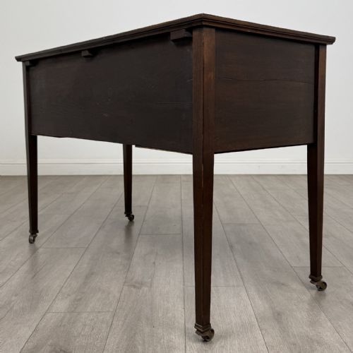 fig 5. An Edwardian mahogany writing table featuring three inlaid drawers, brass drop handles, square tapered legs, and brass castors.
