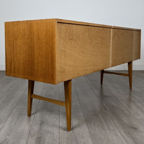 fig 3. A mid-century oak sideboard featuring six wide drawers with circular wooden pull knobs, supported by tapered legs and side stretchers.