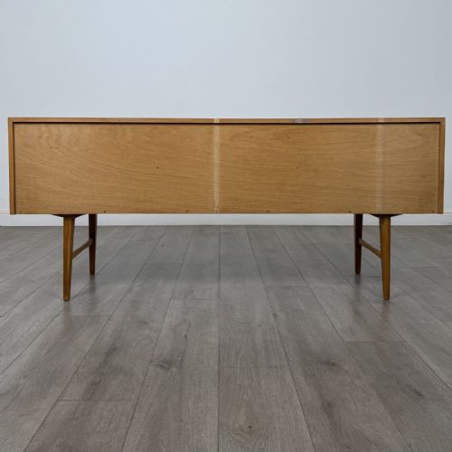 fig 4. A mid-century oak sideboard featuring six wide drawers with circular wooden pull knobs, supported by tapered legs and side stretchers.