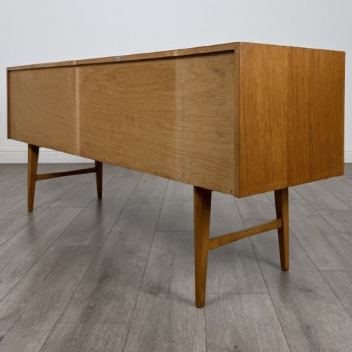 fig 5. A mid-century oak sideboard featuring six wide drawers with circular wooden pull knobs, supported by tapered legs and side stretchers.