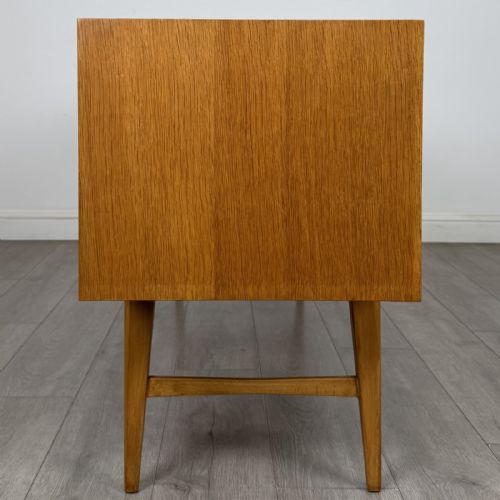 fig 6. A mid-century oak sideboard featuring six wide drawers with circular wooden pull knobs, supported by tapered legs and side stretchers.