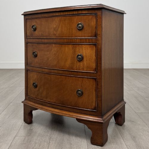 fig 1. A small antique mahogany bow front chest featuring three drawers with brass ring drop handles resting on bracket feet.