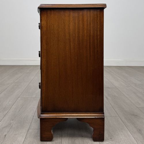 fig 2. A small antique mahogany bow front chest featuring three drawers with brass ring drop handles resting on bracket feet.