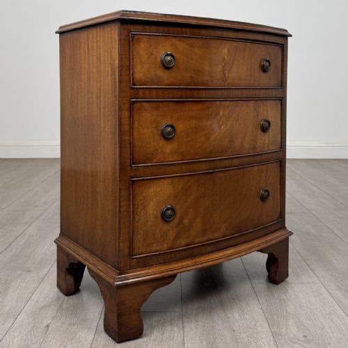 fig 7. A small antique mahogany bow front chest featuring three drawers with brass ring drop handles resting on bracket feet.
