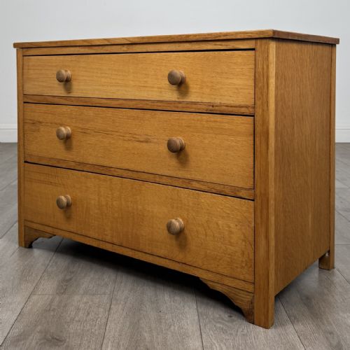 fig 1. A golden oak chest of drawers featuring three horizontal drawers with turned wooden knob handles resting on a shaped apron base.