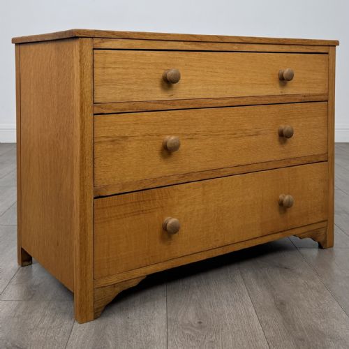 fig 7. A golden oak chest of drawers featuring three horizontal drawers with turned wooden knob handles resting on a shaped apron base.